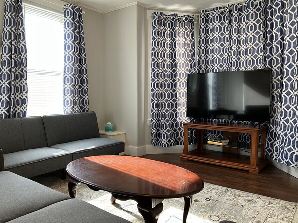 A living room with a grey sofa, a wooden coffee table, and a TV on a wooden stand.