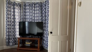Ein Wohnzimmer mit Fernseher auf Holzständer, gemusterten Vorhängen und einem Teppich mit Muster.