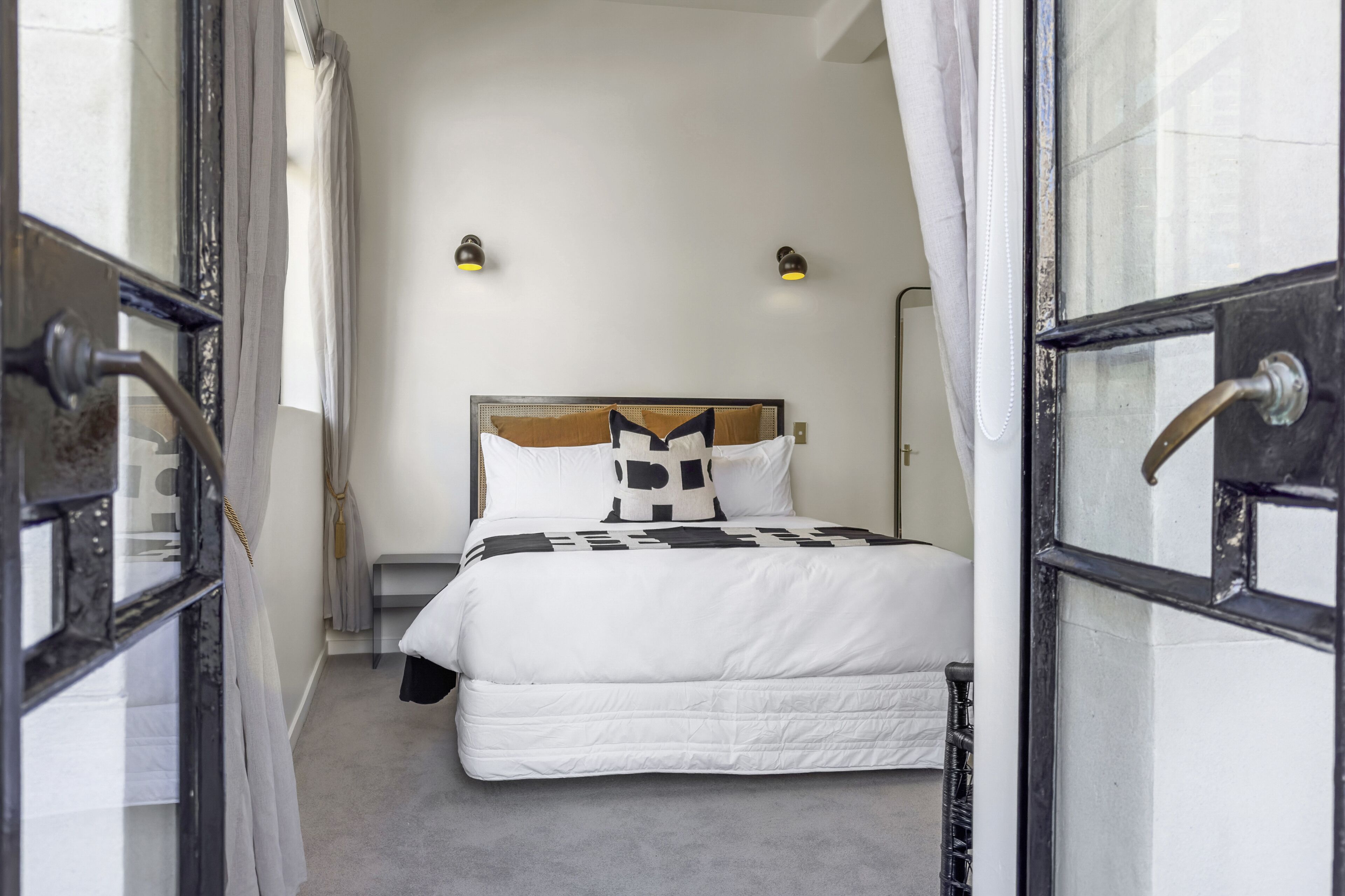 A bedroom with a bed, two bedside lamps, and a window with curtains.