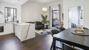 A modern kitchen with a marble island, a dining area with a dark table, and a living space with a sofa and a plant. - Elegant Living in the City (Auckland)