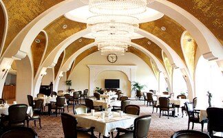 Um amplo salão de banquetes com tetos altos em arco e lustres, com várias mesas e cadeiras para refeições.