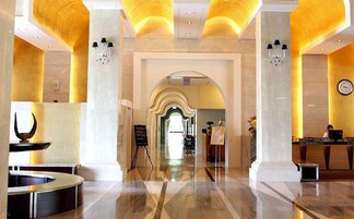 Um hall amplo com piso de mármore, balcão de recepção e um lustre.