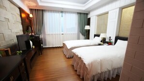 A hotel room with two beds, wooden flooring, a desk with a chair, a TV, and a window with curtains. - Happiness CC Hotel (Naju)