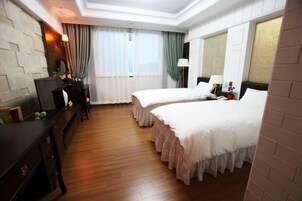 Quarto de hotel com duas camas, piso de madeira, uma escrivaninha com cadeira, televisão e janela com cortinas.