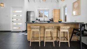 Une cuisine moderne dotée d’un îlot central, de tabourets de bar, d’un réfrigérateur et de luminaires suspendus.