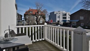 Ein Balkon mit weißer Brüstung, einem Tisch und einem Stuhl, sowie ein Blick auf Gebäude und ein Stoppschild im Hintergrund.