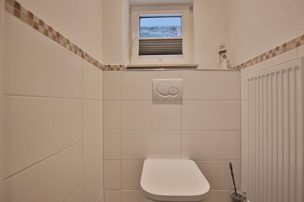 Un baño pequeño con azulejos, inodoro, ventana y radiador.