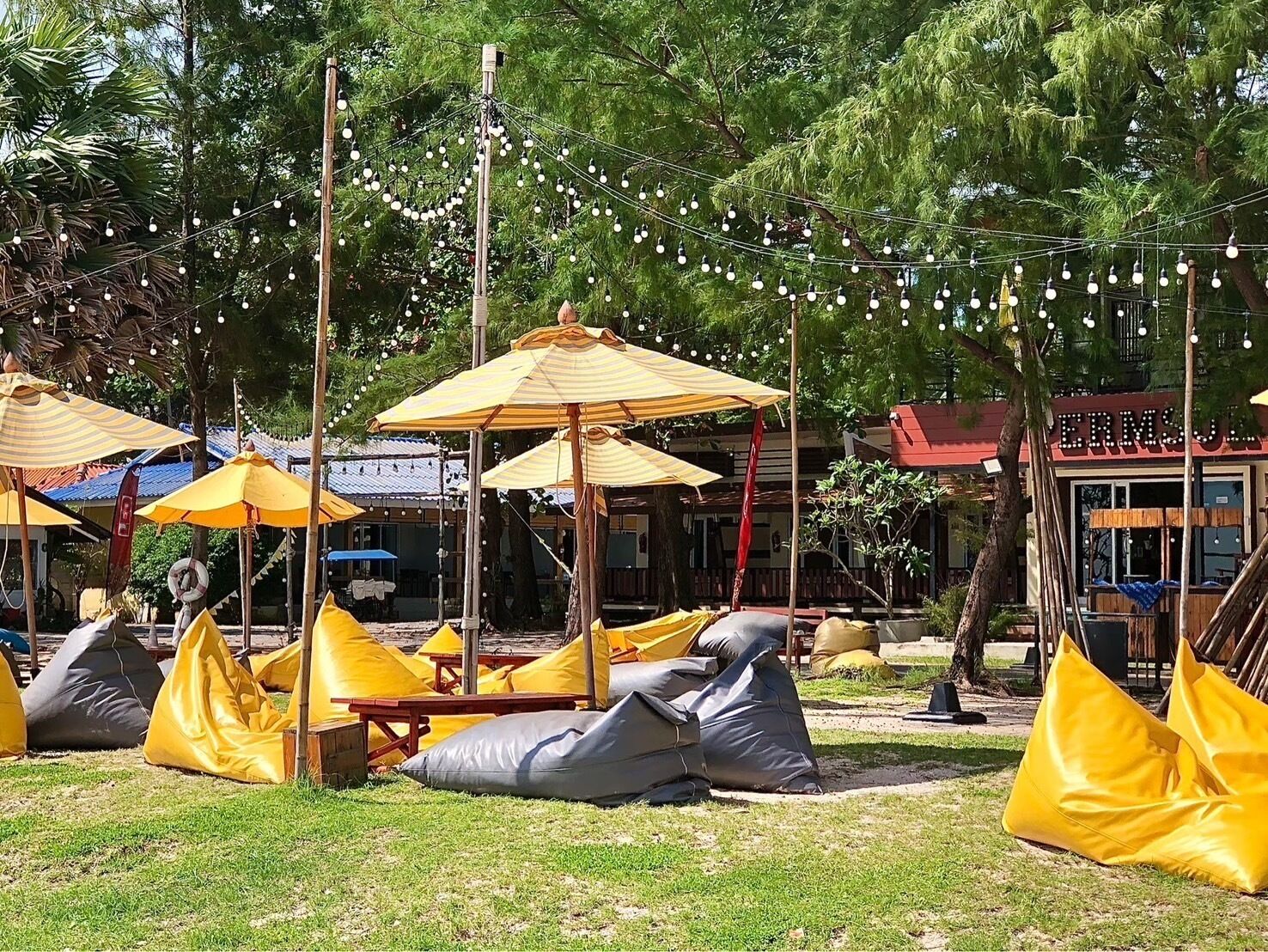 An outdoor seating area with yellow umbrellas and bean bags, surrounded by trees and string lights.