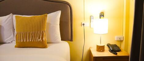 Une chambre d’hôtel comprenant un lit, une table de chevet avec une lampe et un téléphone, et une prise électrique au mur.