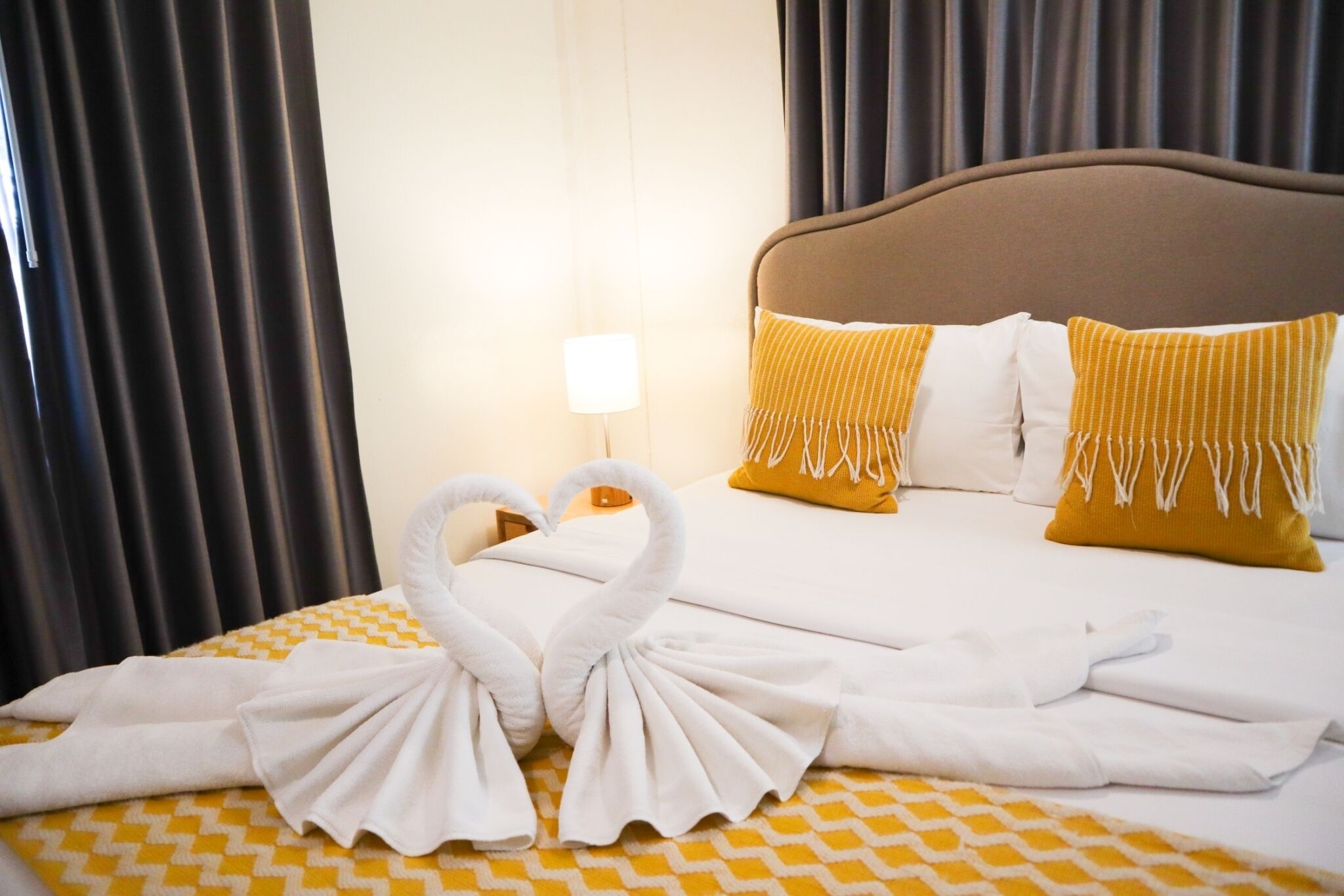 Habitación de hotel con una cama bien hecha, dos almohadas, una lámpara y una ventana con cortinas.