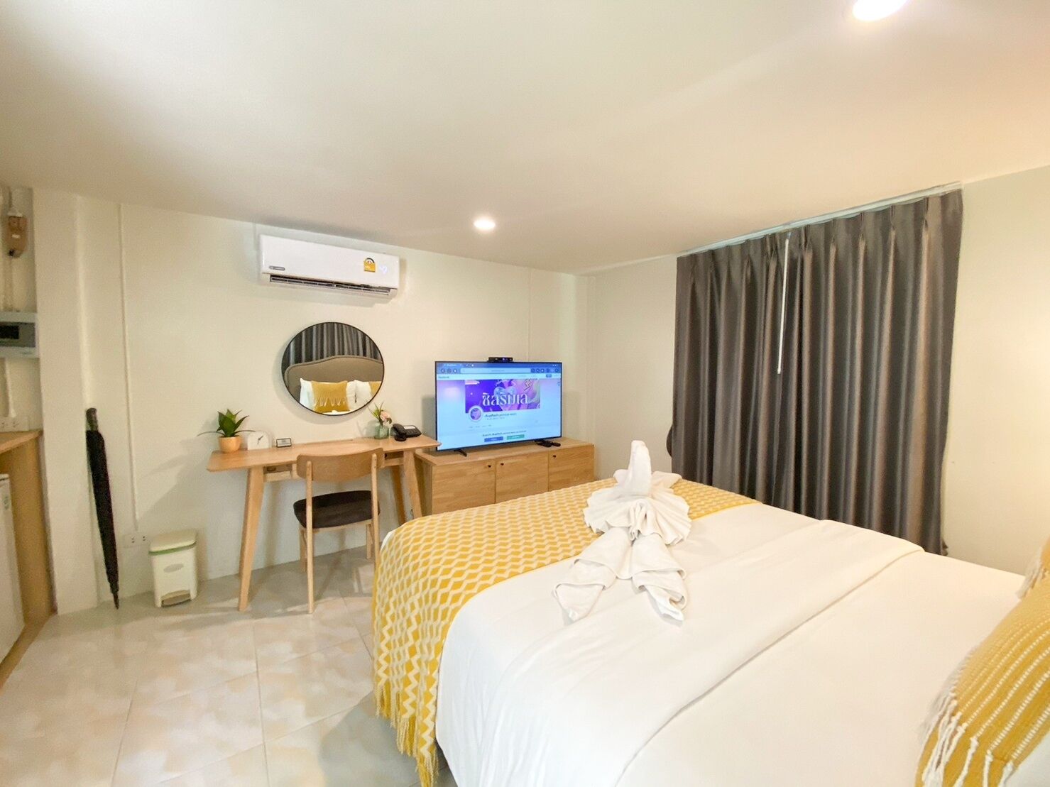 Una habitación de hotel con cama, escritorio con computadora, espejo y aire acondicionado.