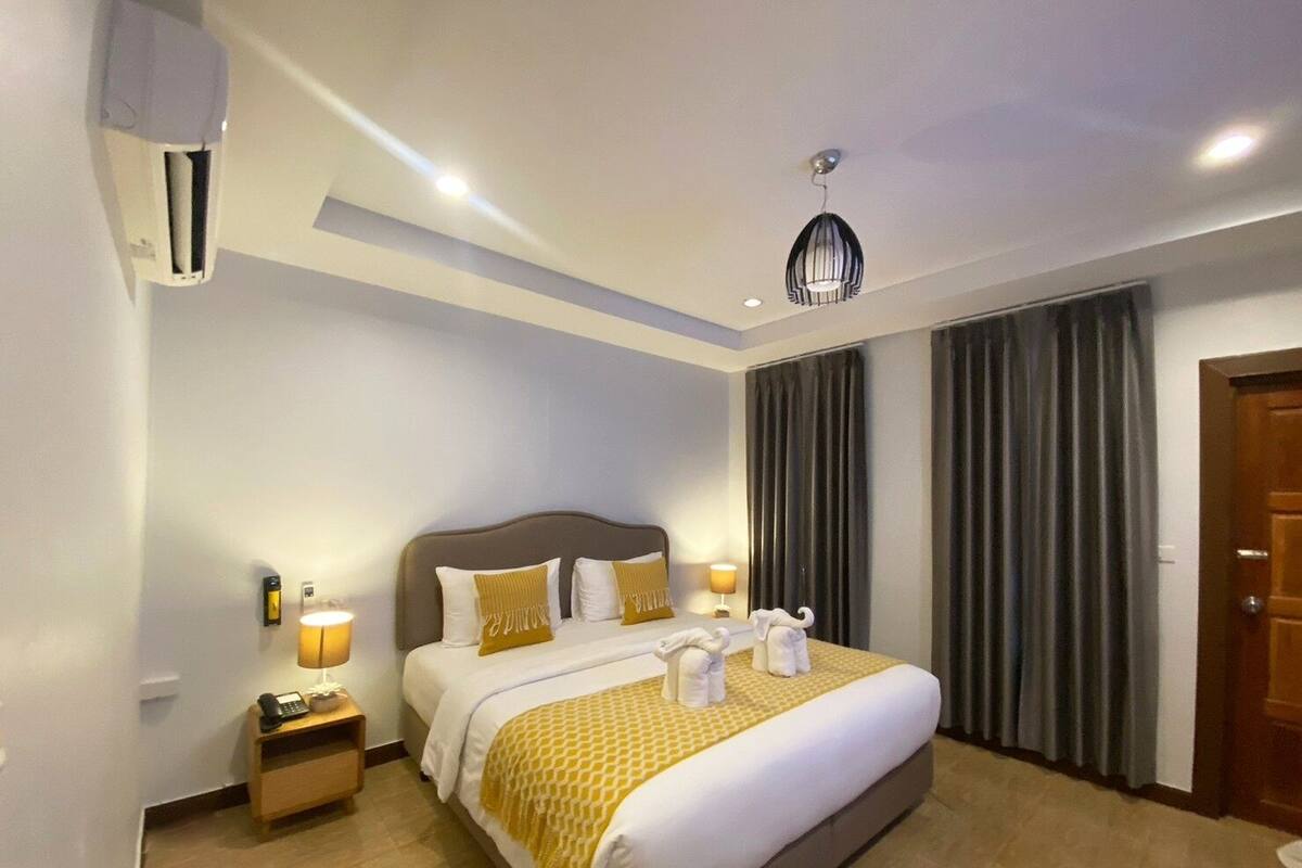 Habitación de hotel con una cama grande, una mesita de noche con lámpara, teléfono y aire acondicionado instalado en la pared.