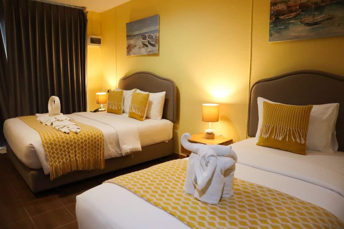 Habitación de hotel con dos camas, cada una con cabecera, mesita de noche con lámpara y una toalla sobre la cama.