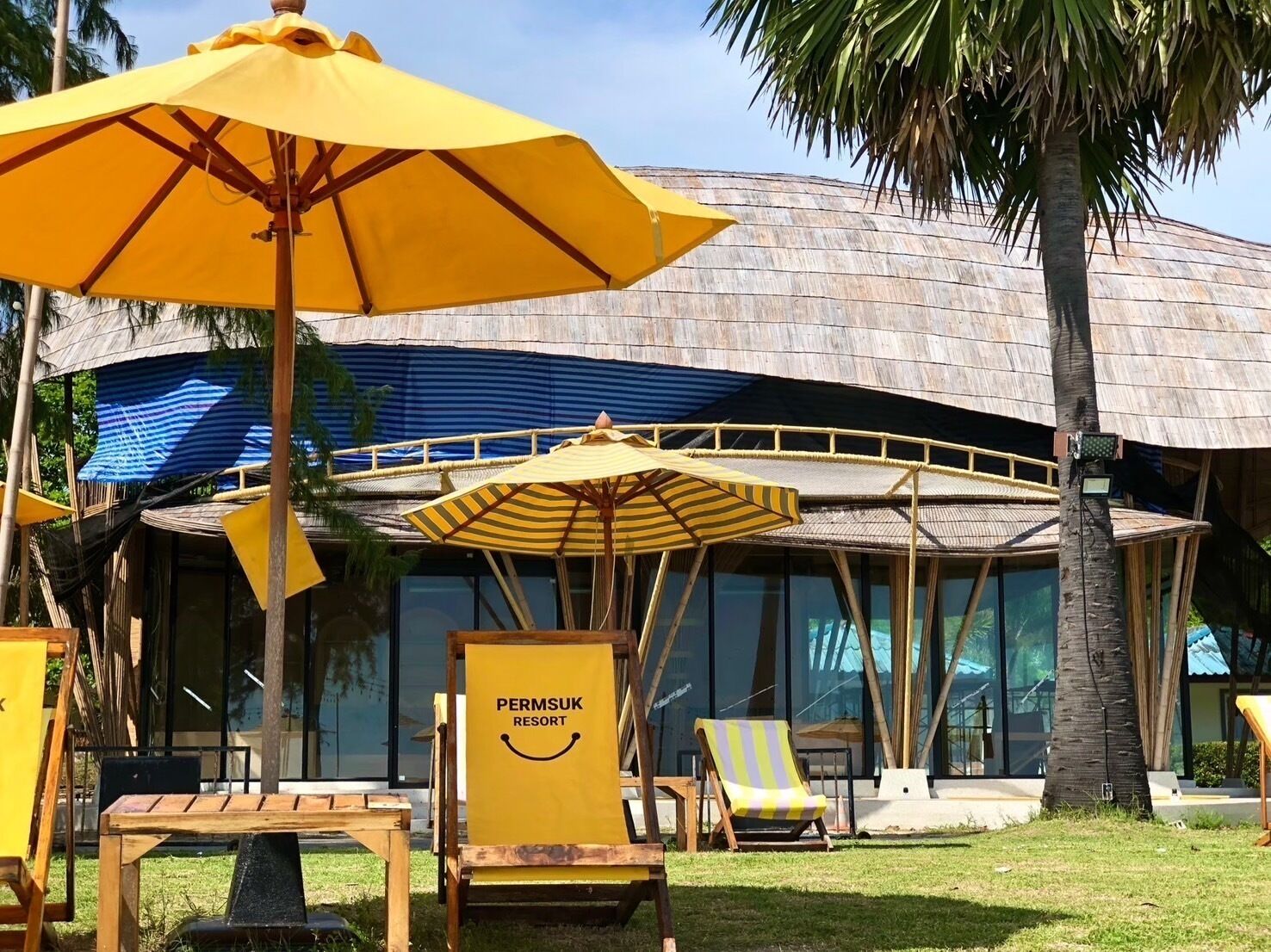 Un resort con techo de paja, asientos al aire libre y un letrero que dice 'PERMSUK RESORT'.