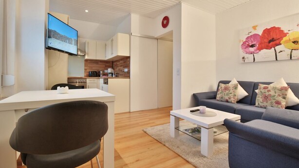 Een moderne woonkamer met een bank, een salontafel en een televisie. Er is een keuken met kasten en een magnetron.