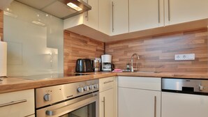 Een moderne keuken met witte kasten, een houten spatwand, een ingebouwde oven, een koffiezetapparaat en een vaatwasser.
