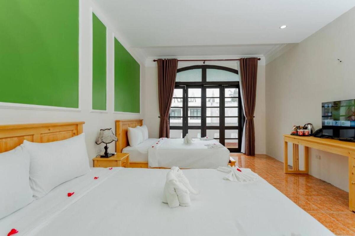 A hotel room with two beds, a television, a desk, and a large window with curtains.