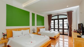 Une chambre d’hôtel avec deux lits, une grande fenêtre avec des rideaux, un bureau en bois et un mur d’accent vert.