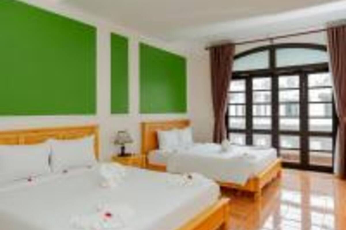 A hotel room with two beds, green walls, a large window with curtains, and a tiled floor.