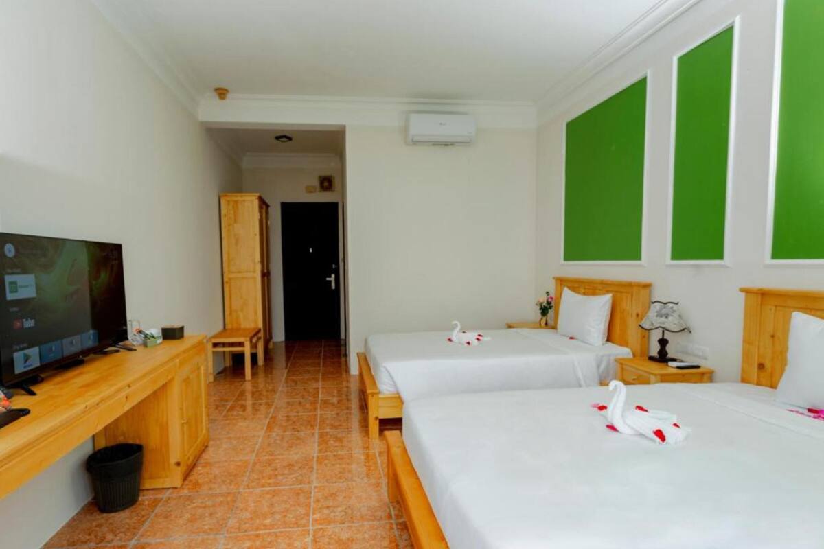 A hotel room with two beds, a TV, a desk, and a bathroom visible in the background.