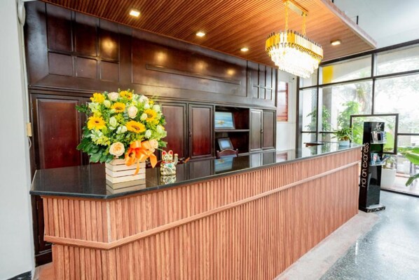 A reception area with a wooden reception desk, a chandelier, and a large window with a view of greenery.