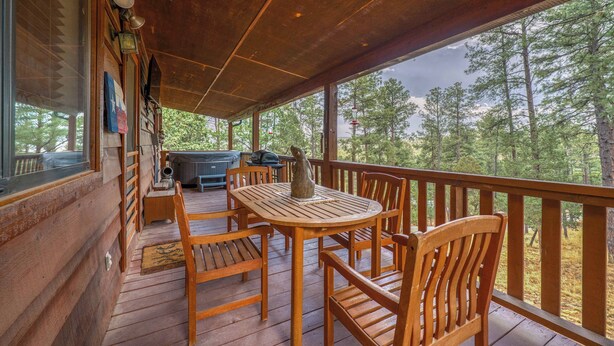 Una terraza de madera con una mesa, sillas, una parrilla y vistas a un bosque.