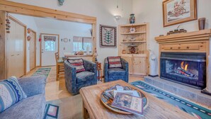 Una sala de estar acogedora con chimenea, dos sillones, una mesa de centro con revistas y un comedor con mesa y sillas.