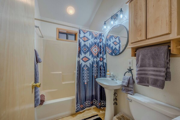 Un baño con cortina de ducha, lavabo, inodoro y un armario de madera.