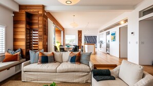 A modern living room with a sectional sofa, a coffee table, and a wooden accent wall. - Oneroa Beach Apartment | You've Got It Maid (Waiheke Island)