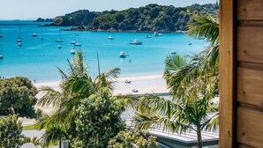 A coastal view with boats on the water, a beach, and a forested hillside. - Oneroa Beach Apartment | You've Got It Maid (Waiheke Island)