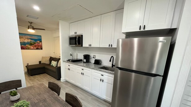 Een moderne keuken met witte kasten, roestvrijstalen apparatuur en een eethoek met een houten tafel en stoelen.