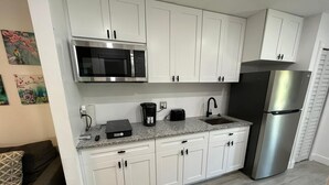 Een moderne keuken met witte kasten, een roestvrijstalen koelkast, een magnetron, een koffiezetapparaat en een broodrooster.