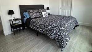 Een slaapkamer met een groot bed, twee nachtkastjes, een deur en een aan de muur bevestigd abstract schilderij.
