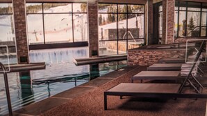 Piscina interior com janelas amplas, paredes de pedra e espreguiçadeiras.
