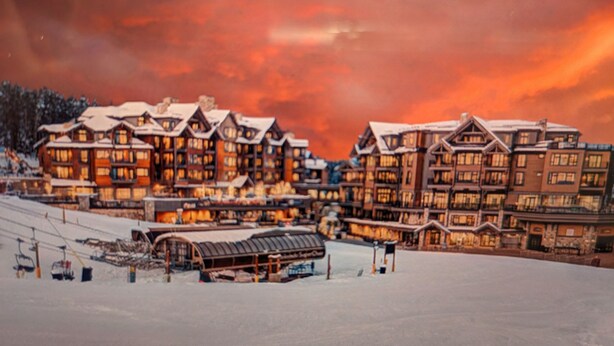 Uma grande pousada com vários edifícios, teleféricos e uma paisagem coberta de neve.
