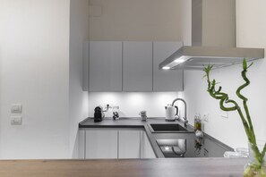 Eine moderne Küche mit weißen Schränken, einer schwarzen Arbeitsplatte, einer Edelstahl-Spüle und einer Kaffeemaschine.