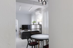 Un salon moderne avec un canapé, un téléviseur, une table à manger avec des chaises et une plante en pot.