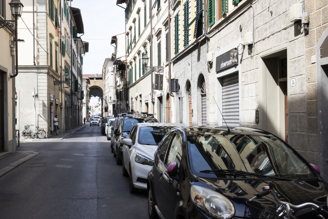 A narrow street lined with parked cars and buildings with shutters.