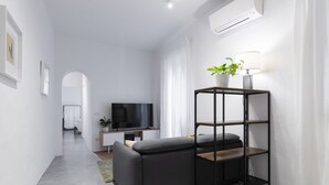 Uma sala de estar moderna com um sofá cinzento, um suporte de TV preto e uma planta numa estante preta.