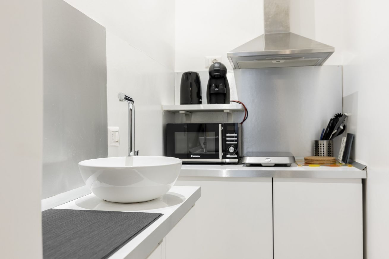 Una cocina moderna con encimera blanca, pileta blanca, microondas, cafetera y tostadora.
