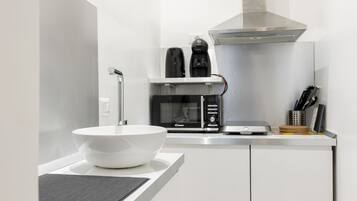 Una cocina moderna con encimera blanca, pileta blanca, microondas, cafetera y tostadora.
