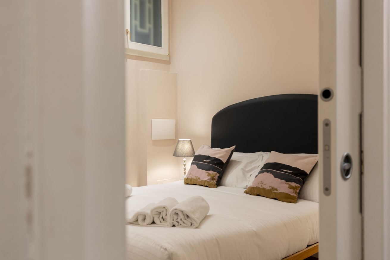 A neatly made bed with a black headboard, a bedside lamp, and a framed picture on the wall.