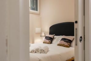 A neatly made bed with a black headboard, a bedside lamp, and a framed picture on the wall.