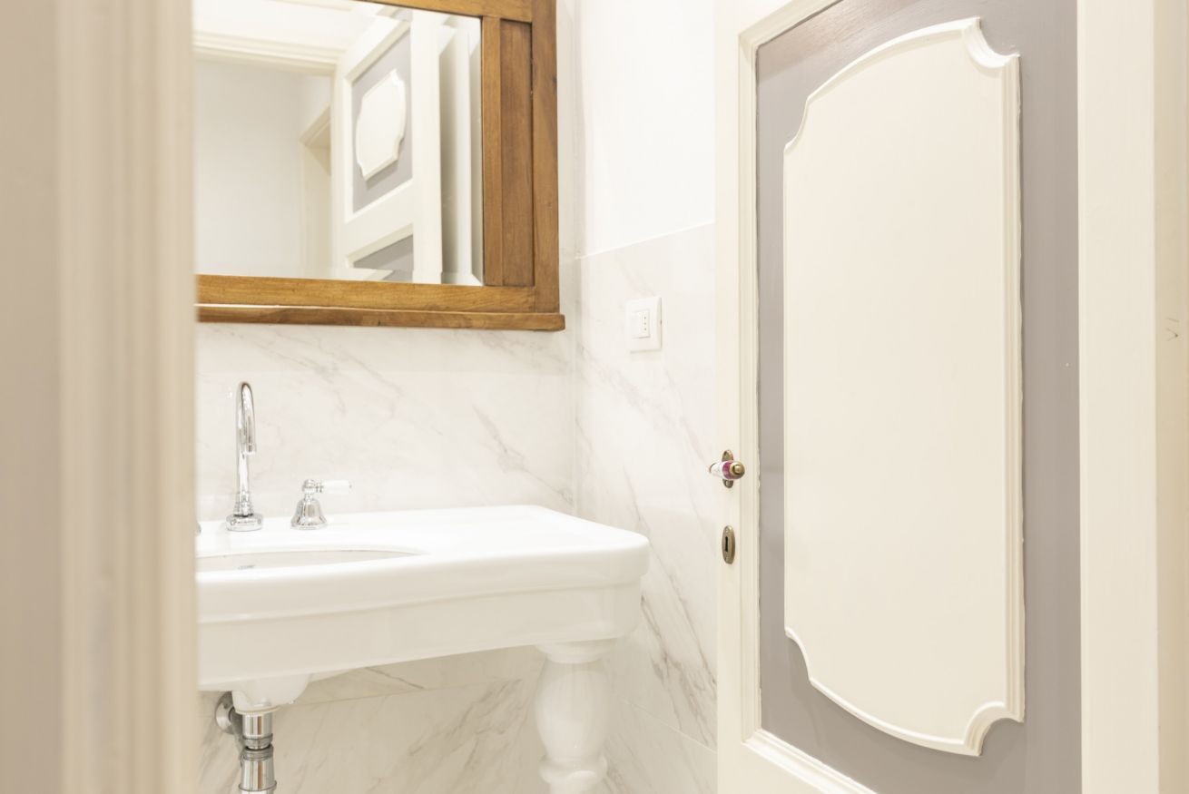 A bathroom with a white sink, a wooden-framed mirror, and a door with a decorative design.