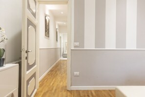 A hallway with wooden flooring, white walls, and a door with a decorative panel.
