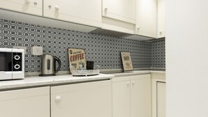 Uma cozinha com armários brancos, micro-ondas, cafeteira e um aviso indicando 'Café fresco servido diariamente'.