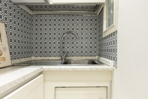A compact kitchen with a patterned backsplash, a stainless steel sink, and a window above the sink.