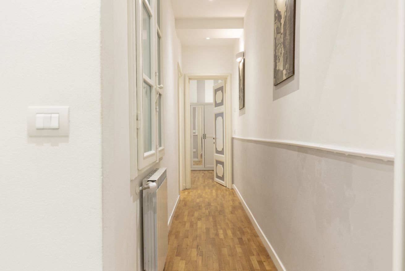 Un pasillo estrecho con suelo de madera, paredes blancas y un radiador.