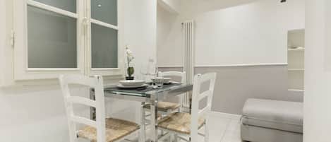 Un coin repas avec une table en verre, des chaises blanches et un canapé gris.