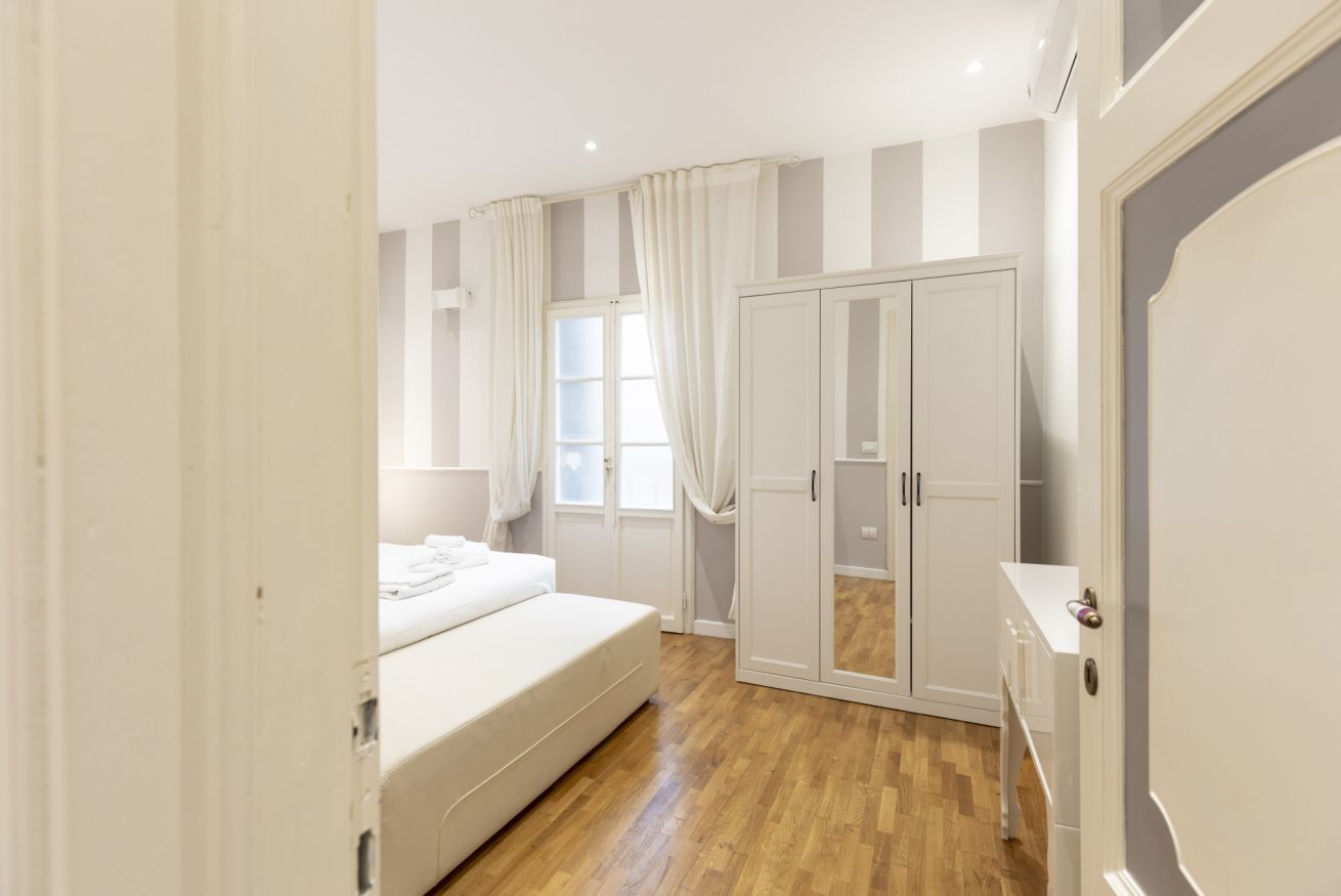 Un dormitorio con cama, armario y ventana con cortinas.